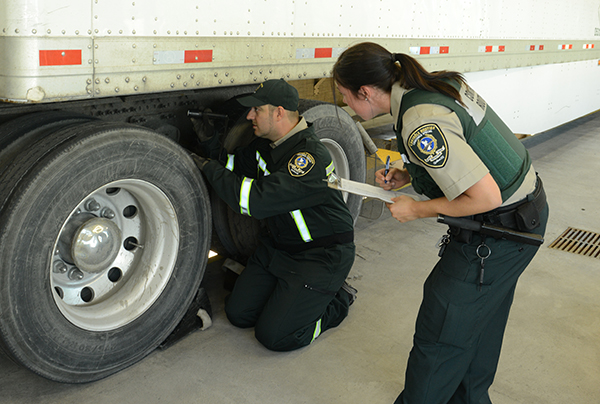 Deux contrôleurs routiers, un homme et une femme, étudient le châssis d’un camion.
