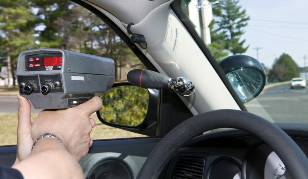 Agent de la paix dans son auto qui tient un pistolet radar.
