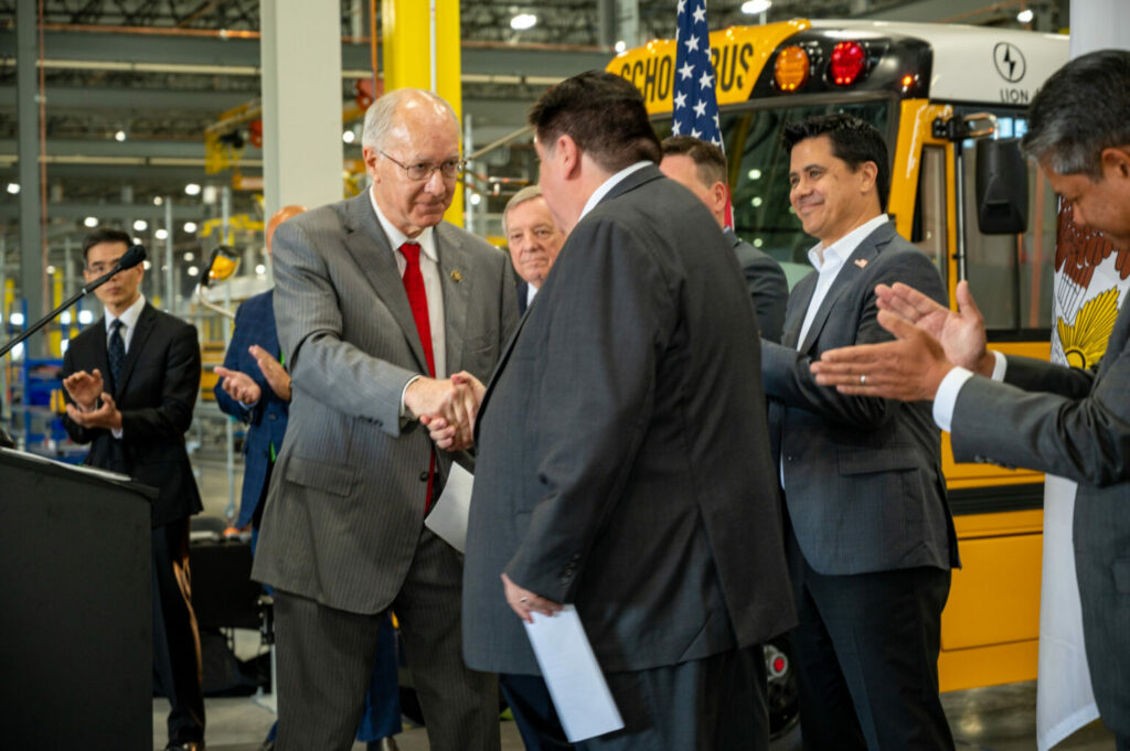 Les politiciens américains Bill Foster et J.B. Pritzker se serrent la main devant un autobus scolaire Lion Électrique lors de la visite de l’usine de Joliet en Illinois le 10 août 22.

