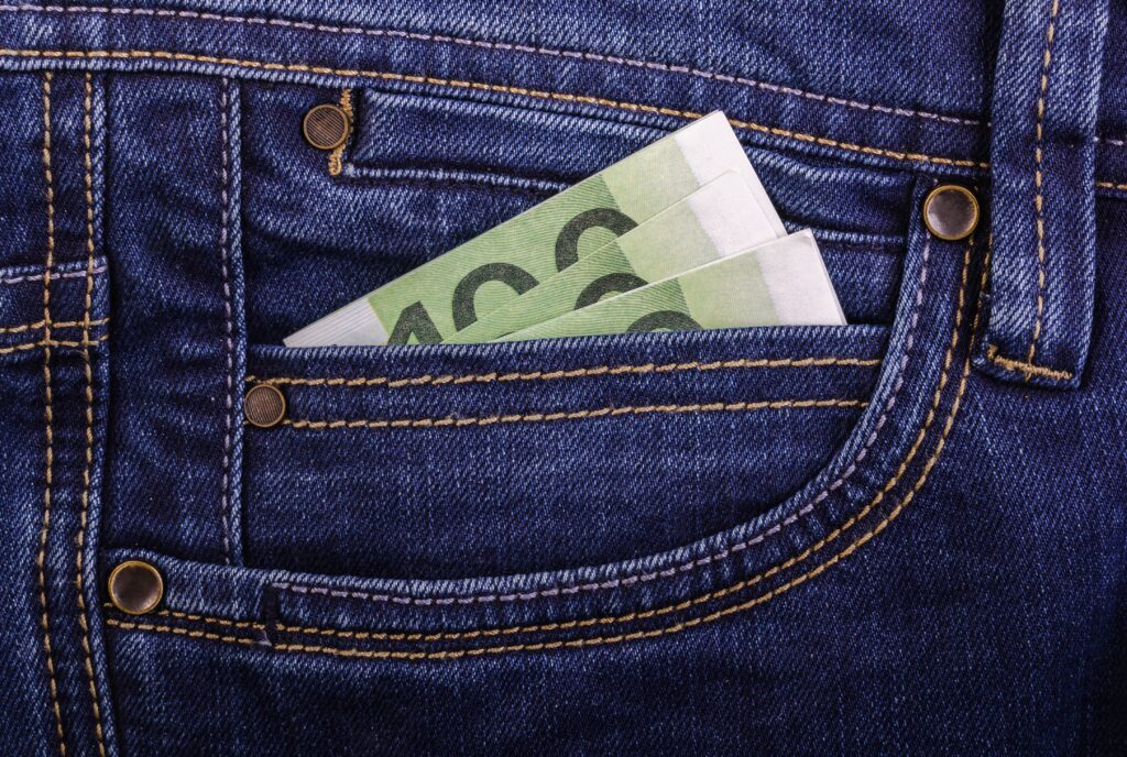Gros plan d’une poche de jean dont sortent des billets de banque.
