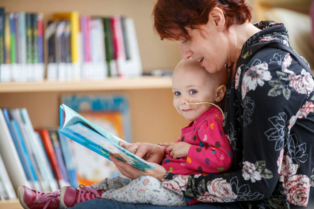 Femme lit un livre à un jeune enfant atteint de cancer qui a perdu ses cheveux.
