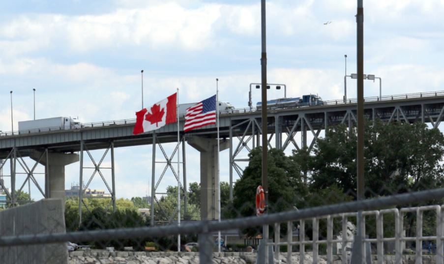 Deux camions traversent la frontière. Drapeaux des États-Unis et du Canada.
