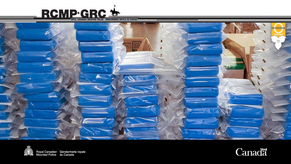 Piles de sachets de cocaïne présumée devant une affiche de la GRC.
