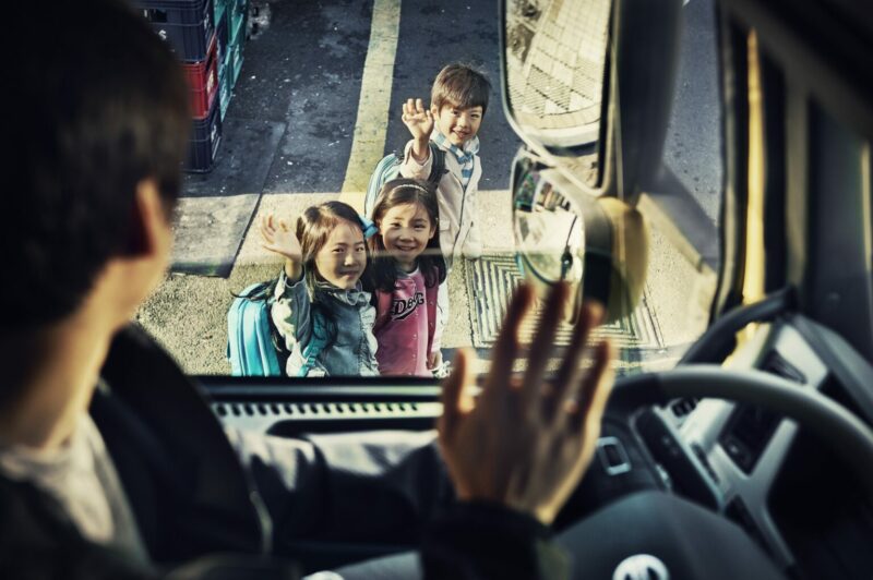 Chauffeur dans sa cabine envoie la main à des enfants sur le trottoir.