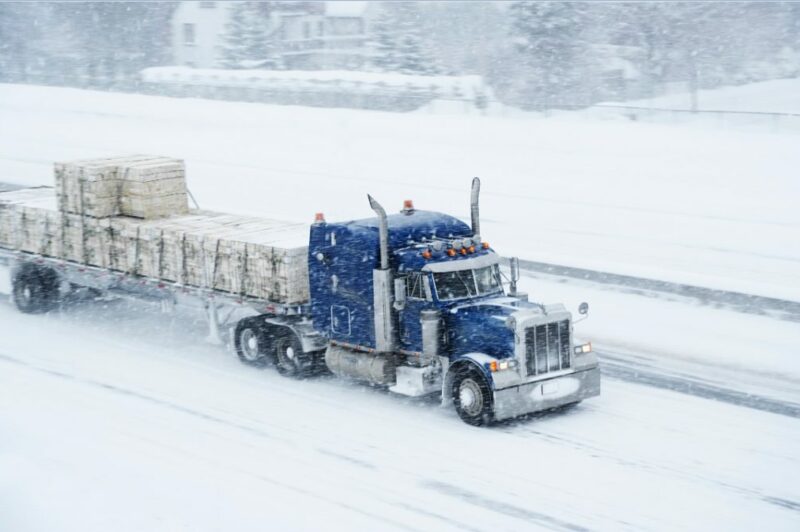 Camion avec remorque plateforme en pleine tempête de neige