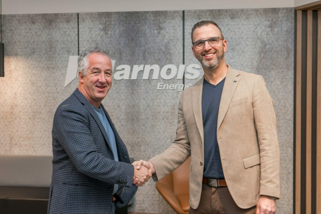 Serge Harnois et Marquis Grégoire se serrent la main devant un logo Harnois Énergies